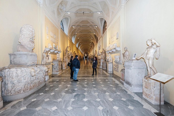 Visitors walking through a Vatican Museums sculpture corridor