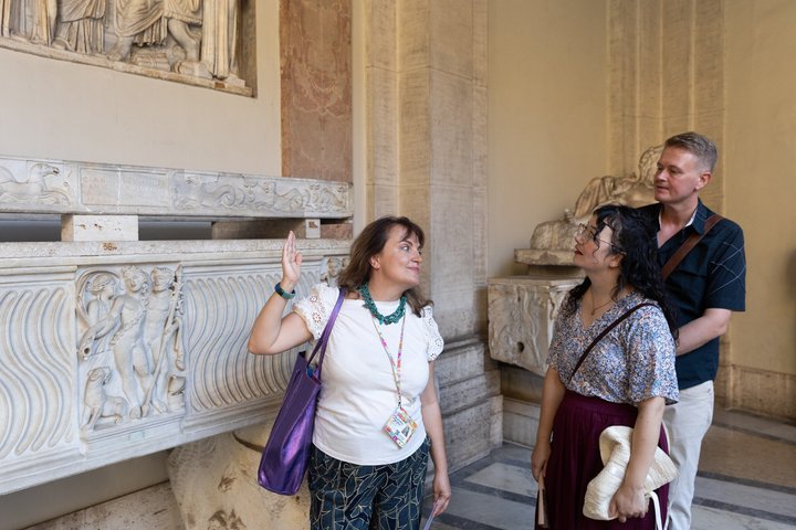 A guide and visitors beside a carved marble sarcophagus